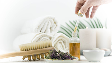 Spa treatment bottle of natural organic oil essence serum collagen. Towel, aromatic candles, flowers, massage brush and Buddha on white background. Copy space for text. Beautiful woman hands. Oil drop