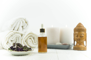 Obraz na płótnie Canvas Spa treatment bottle of natural organic oil essence serum collagen. Towel, aromatic candles, flowers, massage brush and Buddha on white background. Copy space for text. Beautiful woman hands. Oil drop