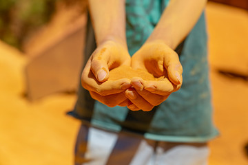 Joined dirty hands closed fingers as a cup with yellow ochre powder dirt dust sand close up...