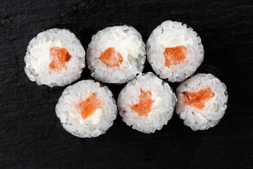 Maki Sushi Rolls with salmon on black stone on dark background. Sushi menu. Japanese food. Closeup of delicious japanese food with sushi roll. Horizontal photo