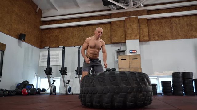 Fit muscular man doing crossfit exercises working out lifting a large rubber tyre in a gym