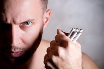 stern man angrily looks at the camera, clenching cigarettes in his fist