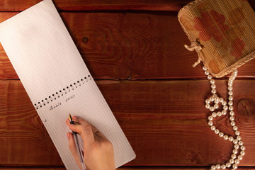 Female hand holding pen on open notepad. Woman writes goals for new year 2020. Pearl necklace on a...