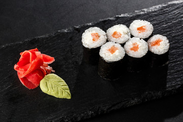 Maki Sushi Rolls with salmon on black stone on dark background. With ginger and wasabi. Sushi menu. Japanese food. Closeup of delicious japanese food with sushi roll. Horizontal photo