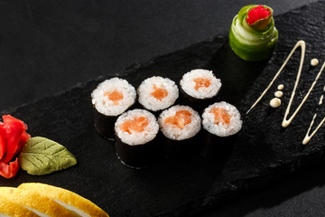 Maki Sushi Rolls with salmon on black stone on dark background. With ginger and wasabi. Sushi menu. Japanese food. Closeup of delicious japanese food with sushi roll. Horizontal photo