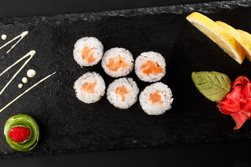 Maki Sushi Rolls with salmon on black stone on dark background. With ginger and wasabi. Sushi menu. Japanese food. Closeup of delicious japanese food with sushi roll. Horizontal photo