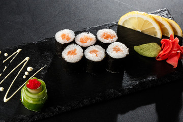 Maki Sushi Rolls with salmon on black stone on dark background. With ginger and wasabi. Sushi menu. Japanese food. Closeup of delicious japanese food with sushi roll. Horizontal photo