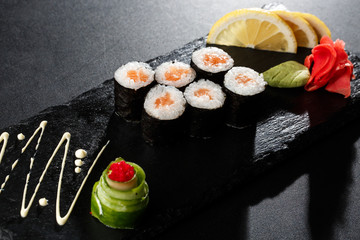 Maki Sushi Rolls with salmon on black stone on dark background. With ginger and wasabi. Sushi menu. Japanese food. Closeup of delicious japanese food with sushi roll. Horizontal photo