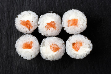 Maki Sushi Rolls with salmon on black stone on dark background. Sushi menu. Japanese food. Closeup of delicious japanese food with sushi roll. Horizontal photo