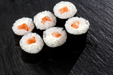 Maki Sushi Rolls with salmon on black stone on dark background. Sushi menu. Japanese food. Closeup of delicious japanese food with sushi roll. Horizontal photo