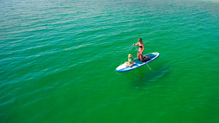Little girl in a life vest sitting on the paddle board with mother