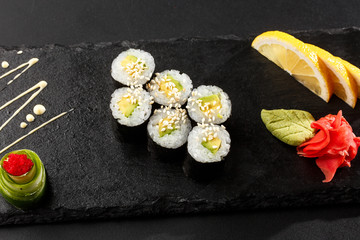Obraz na płótnie Canvas Maki Sushi Rolls with cucumber or avocado on black stone on dark background. Sushi menu. Japanese food. Closeup of delicious japanese food with sushi roll. Horizontal photo