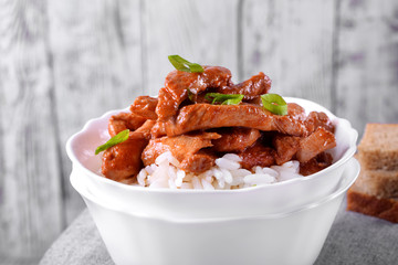 Pieces of meat in tomato sauce with spices on rice in a white bowl