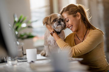 Young happy woman cuddling her dog in the office.