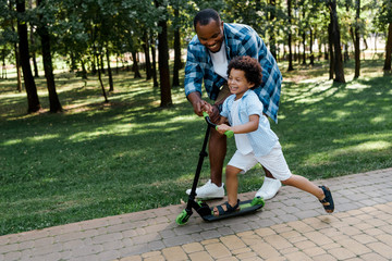 cheerful african american father near happy kid on scooter