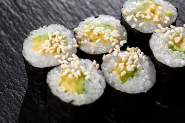 Maki Sushi Rolls with cucumber or avocado on black stone on dark background. Sushi menu. Japanese food. Closeup of delicious japanese food with sushi roll. Horizontal photo