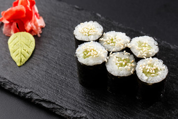 Maki Sushi Rolls with cucumber or avocado on black stone on dark background. Sushi menu. Japanese food. Closeup of delicious japanese food with sushi roll. Horizontal photo