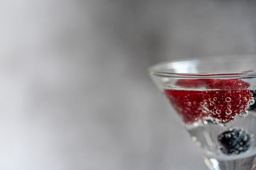 Berries soda water. Summer juice with fresh raspberries in a glass on a gray background. Raspberry cold refreshing cocktail. copy space.