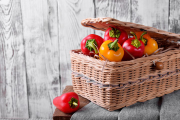 Fototapeta na wymiar Little red and yellow bell peppers in a wicker basket against white wooden background