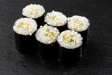 Maki Sushi Rolls with cucumber or avocado on black stone on dark background. Sushi menu. Japanese food. Closeup of delicious japanese food with sushi roll. Horizontal photo