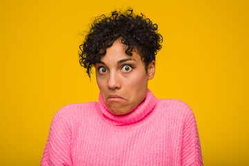 Young african american woman wearing a pink sweater shrugs shoulders and open eyes confused.