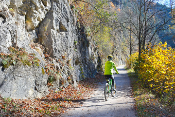 Obraz premium Woman is riding a bicycle along Dunajec river in autumn sunny day, Pieniny mountains