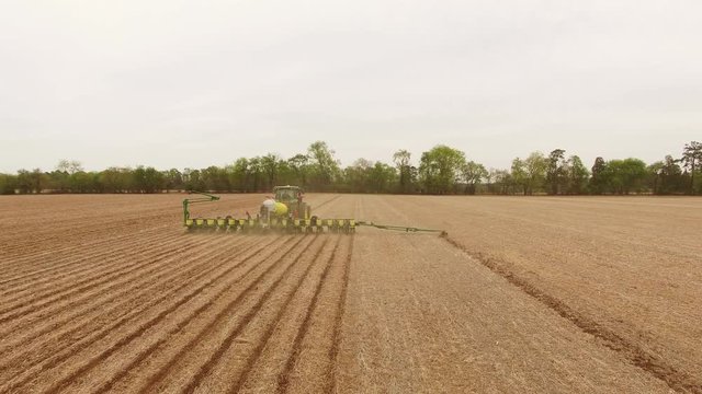 Green tractor tills field in Virginia, aerial