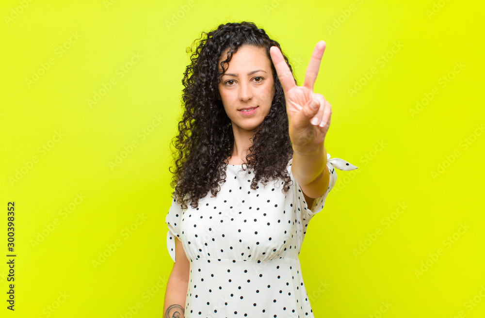 Wall mural young pretty woman smiling and looking friendly, showing number two or second with hand forward, cou