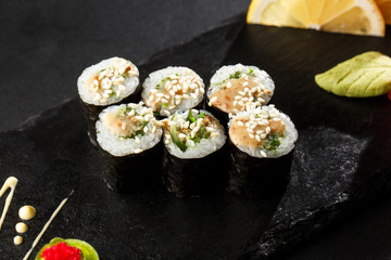Maki Sushi Rolls with wakame and nut sauce on black stone on dark background. Sushi menu. Japanese food. Closeup of delicious japanese food with sushi roll. Horizontal photo