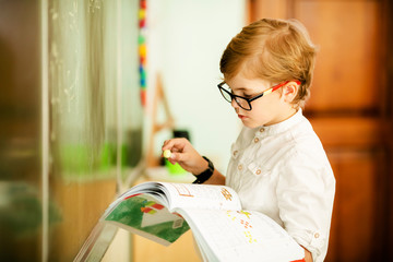adorable blonde american primary school student with big glasses studying in classroom