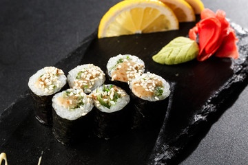 Fototapeta na wymiar Maki Sushi Rolls with wakame and nut sauce on black stone on dark background. Sushi menu. Japanese food. Closeup of delicious japanese food with sushi roll. Horizontal photo