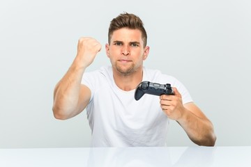 Young man holding a game controller showing fist to camera, aggressive facial expression.