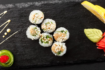 Maki Sushi Rolls with wakame and nut sauce on black stone on dark background. Sushi menu. Japanese food. Closeup of delicious japanese food with sushi roll. Horizontal photo