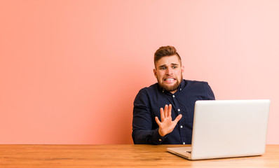 Young man working with his laptop rejecting someone showing a gesture of disgust.