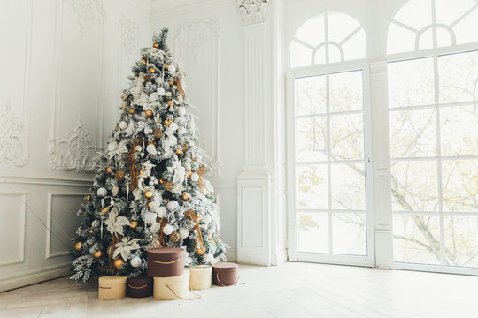 Classic christmas New Year decorated interior room New year tree. Christmas tree with gold decorations. Modern white classical style interior design apartment, large window. Christmas eve at home