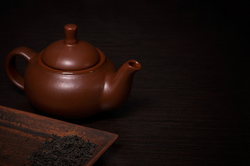 Clay teapot on a dark wooden table. Nearby are tea leaves on a plate.