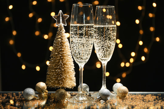 Champagne glasses and baubles against blurred lights background, space for text