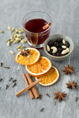christmas and seasonal drinks concept - hot mulled wine, dry orange slices, raisins with cashew nuts and aromatic spices on grey background