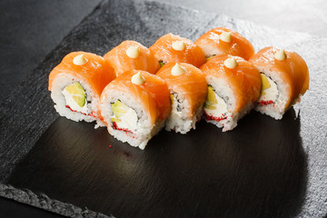 Sushi Rolls with salmon, avocado, flying fish caviar and Cream Cheese inside on black slate isolated. Philadelphia roll sushi with salmon. Sushi menu. Horizontal photo.