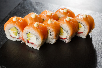 Sushi Rolls with salmon, avocado, flying fish caviar and Cream Cheese inside on black slate isolated. Philadelphia roll sushi with salmon. Sushi menu. Horizontal photo.