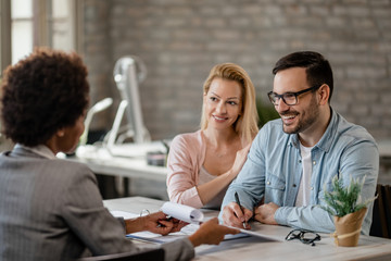 Happy couple signing an agreement on a meeting with insurance agent.