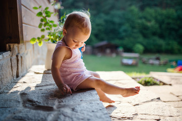 A cute toddler girl sitting outdoors in front of house in summer.