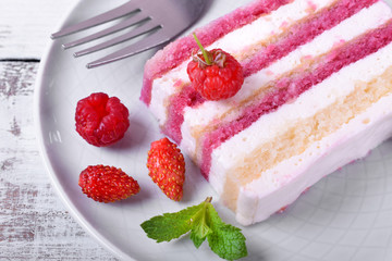 Piece of cake with many layers topped with fresh berries and mint on a ceramic plate