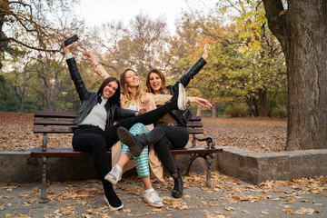 Three young adult females having fun in the park, cheering and laughing while sitting on the bench 