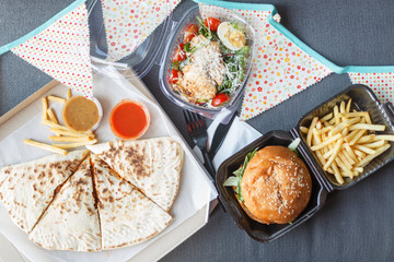 Appetizing pizza, sandwiches and burgers and fried potatoes on a white wooden table. Fast food concept. Top view