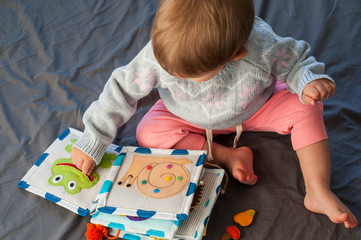 Baby girl playing with her textile book. Page with felt frog and snail. Woolly toys. Baby development. Educational toys. Fine motor skills. Little colorful buttons.