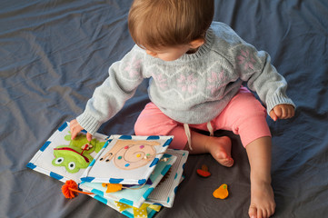 Baby girl playing with her textile book. Page with felt frog and snail. Woolly toys. Baby...