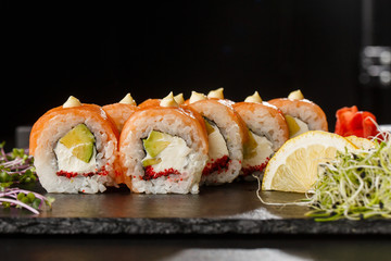 Sushi Rolls with salmon, avocado, flying fish caviar and Cream Cheese inside on black slate isolated. Philadelphia roll sushi with salmon. Sushi menu. Horizontal photo.