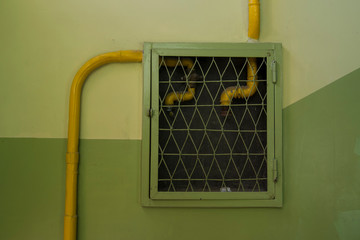 Yellow pipes behind the grid on the green wall, staircase, corridor