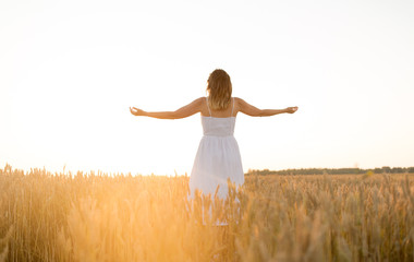 Naklejka na ściany i meble nature, people and happiness concept - happy young woman in white dress and enjoying freedom on cereal field in summer